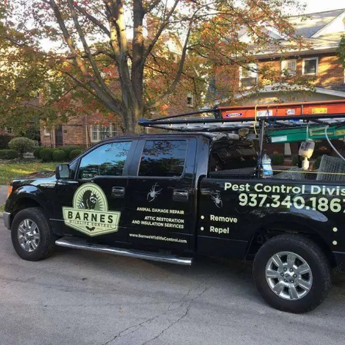 A Barnes Wildlife Control service vehicle parked in front of a home while technicians perform wildlife control and removal services